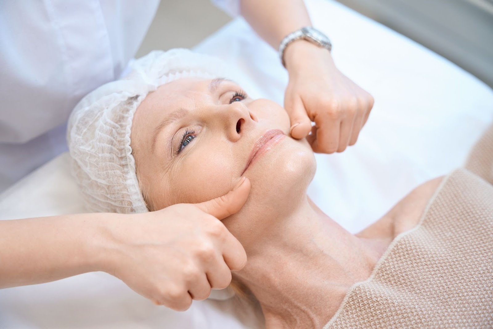 Mature woman in a cosmetic cap getting a lymphatic facial massage to improve circulation and skin firmness