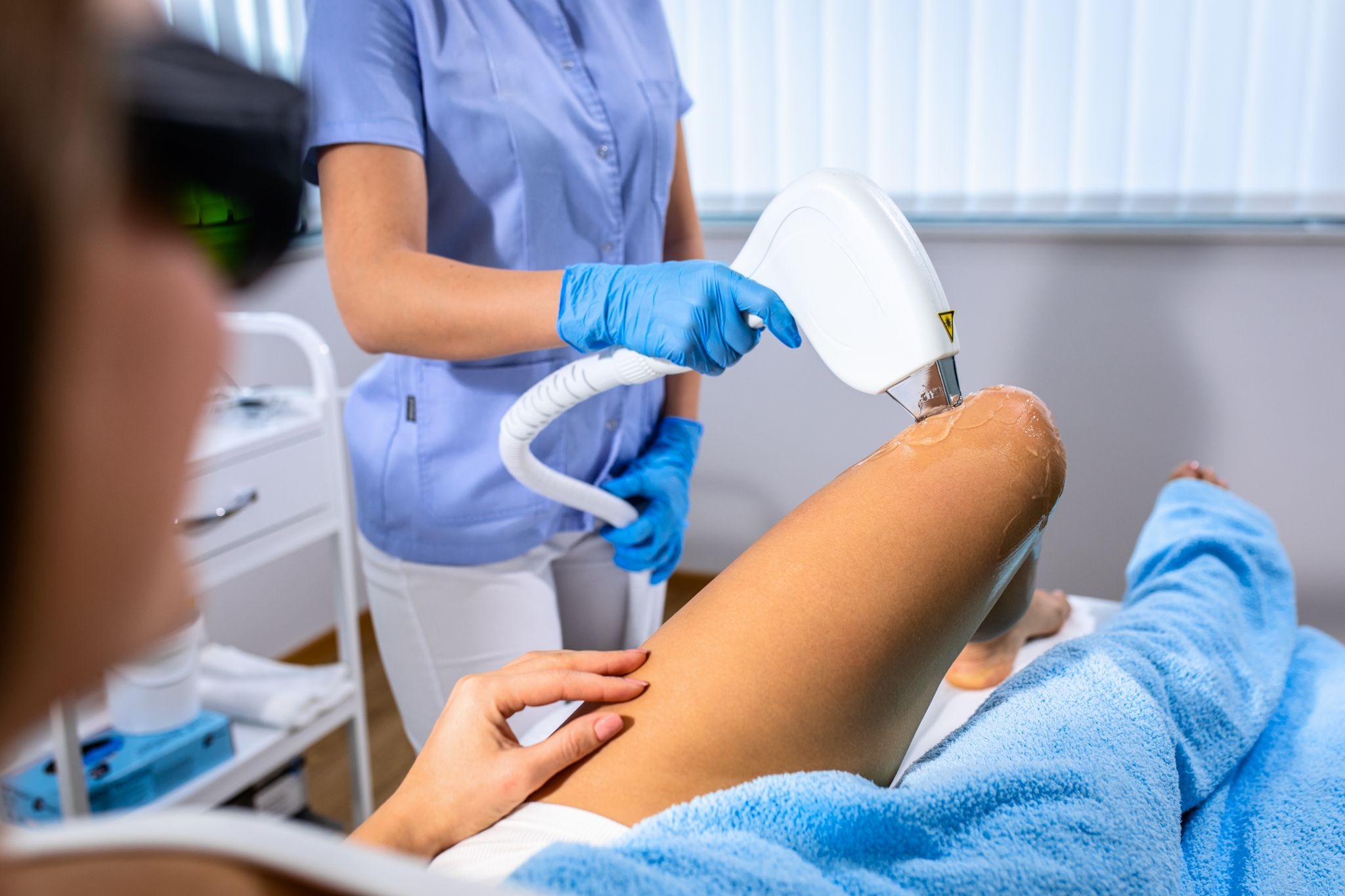 Aesthetic specialist using a laser device for leg hair removal treatment on a female client