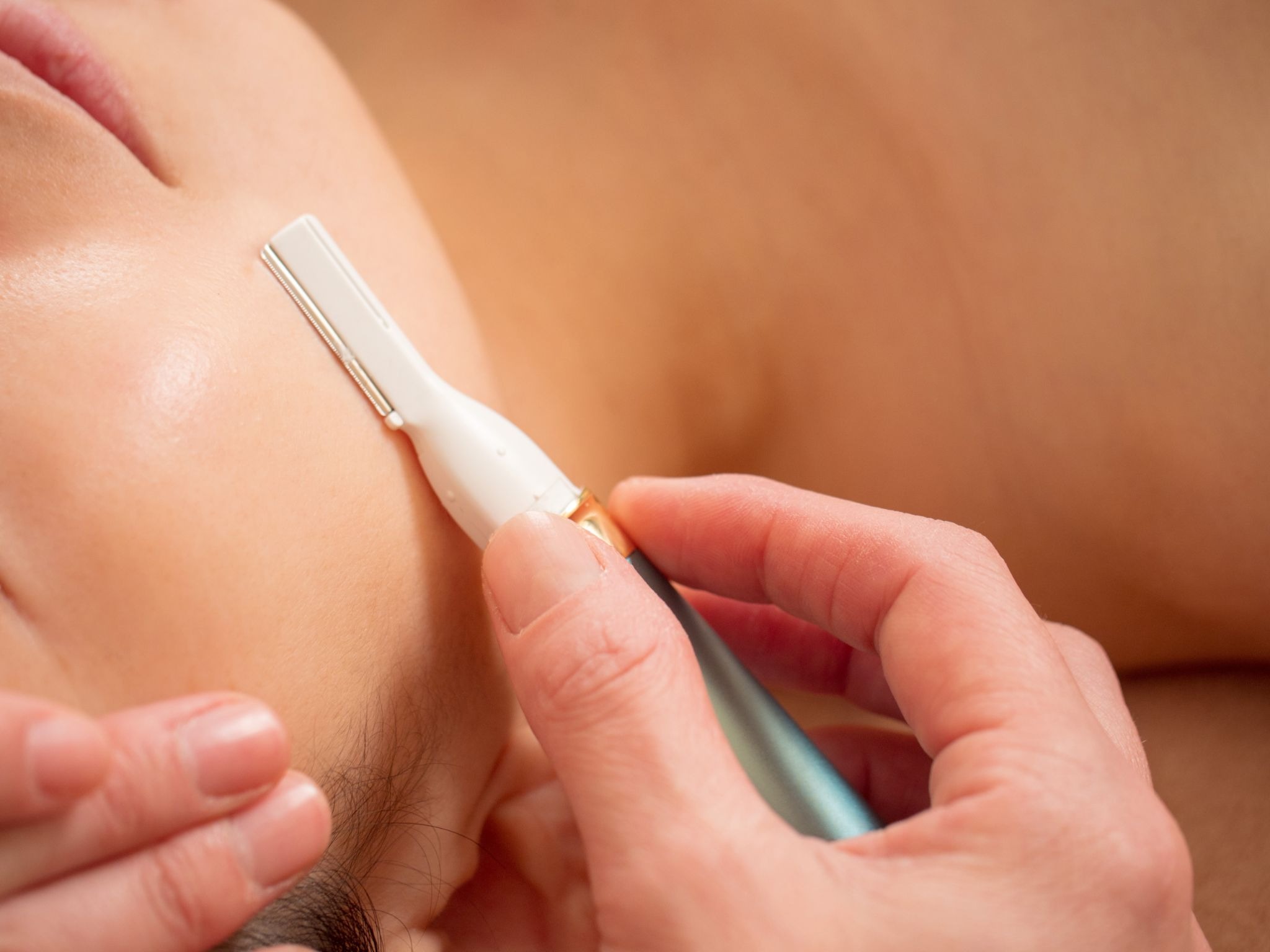 Detailed view of a blade removing fine facial hair and skin from a woman’s face