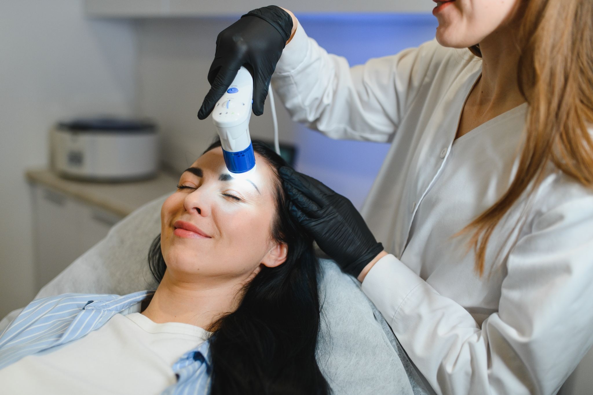 An esthetician performing laser treatment on a woman’s forehead