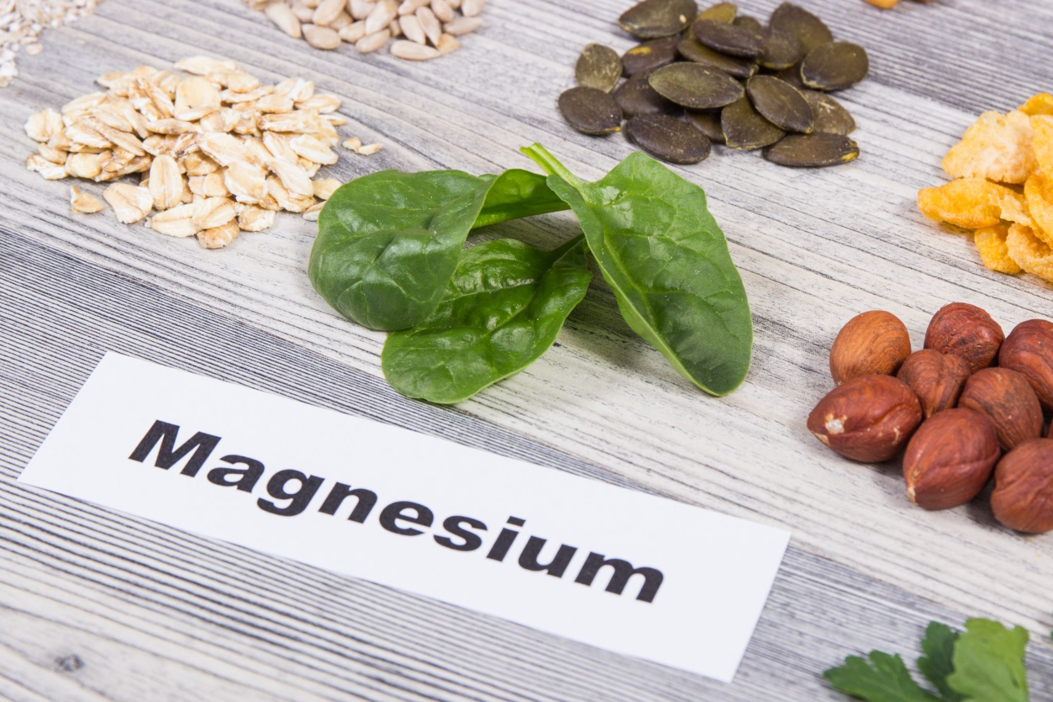 Assorted magnesium-rich foods on a wooden table with the word “magnesium” displayed beside them