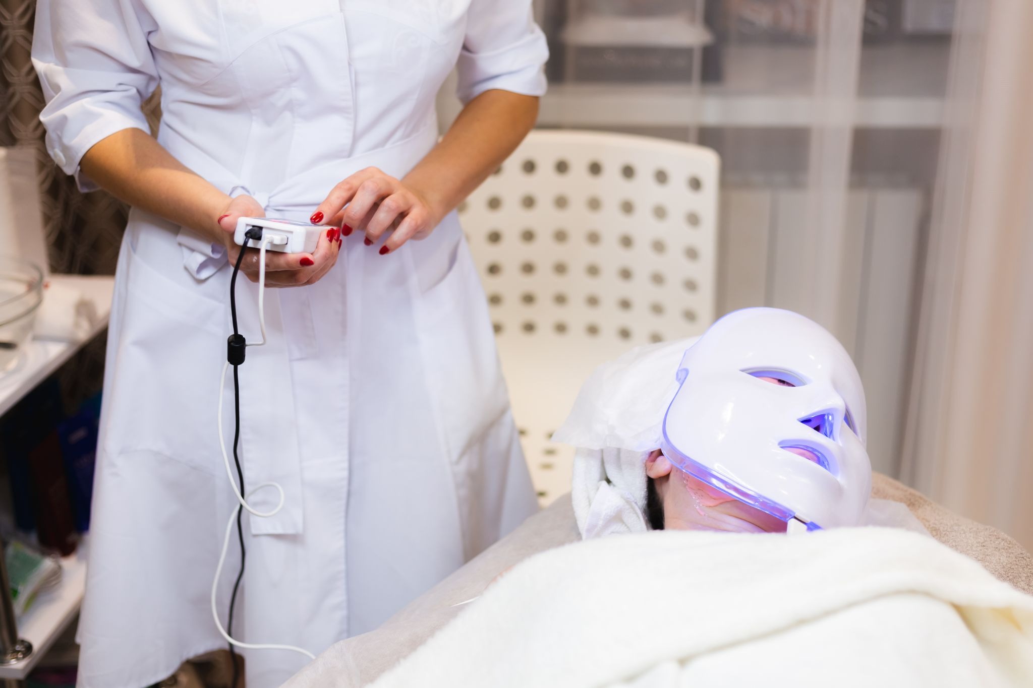 Woman receiving LED facial treatment mask for acne-prone skin