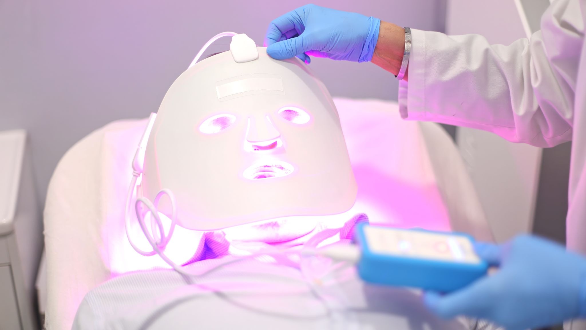 A skincare professional adjusting an LED light therapy mask on a patient during a skincare treatment