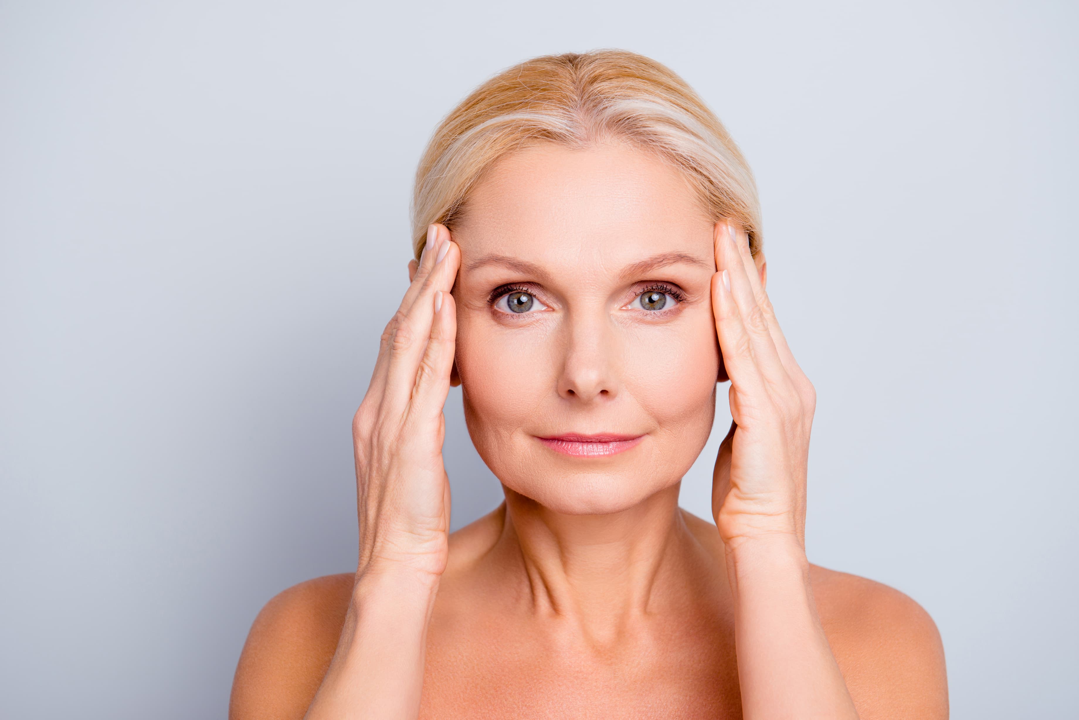 Woman over 45 with smooth, healthy-looking skin gently touching her temples