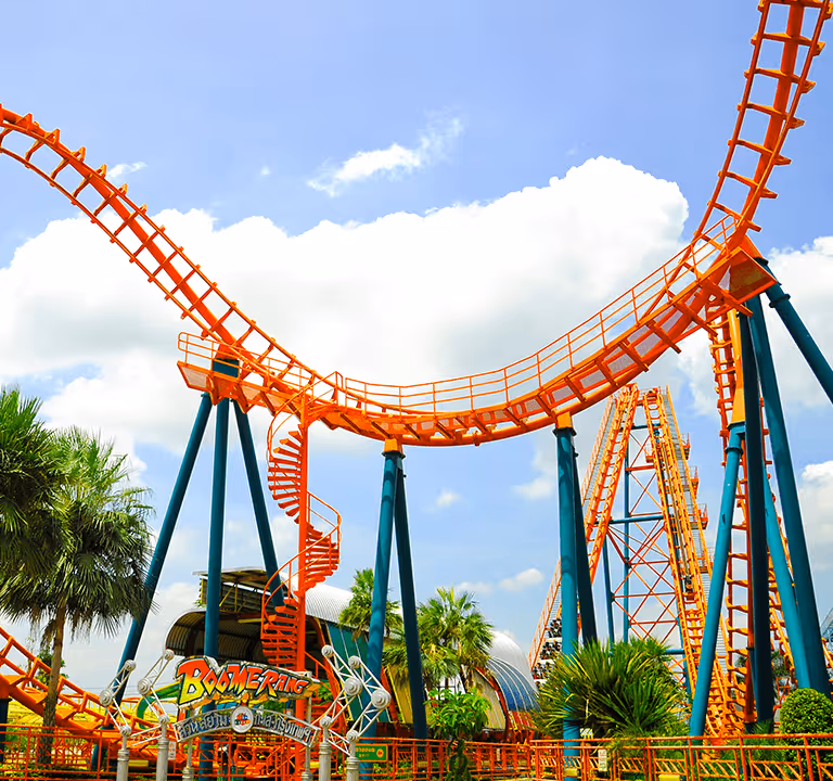 Bright orange roller coaster track looping and twisting at an amusement park under a blue sky.