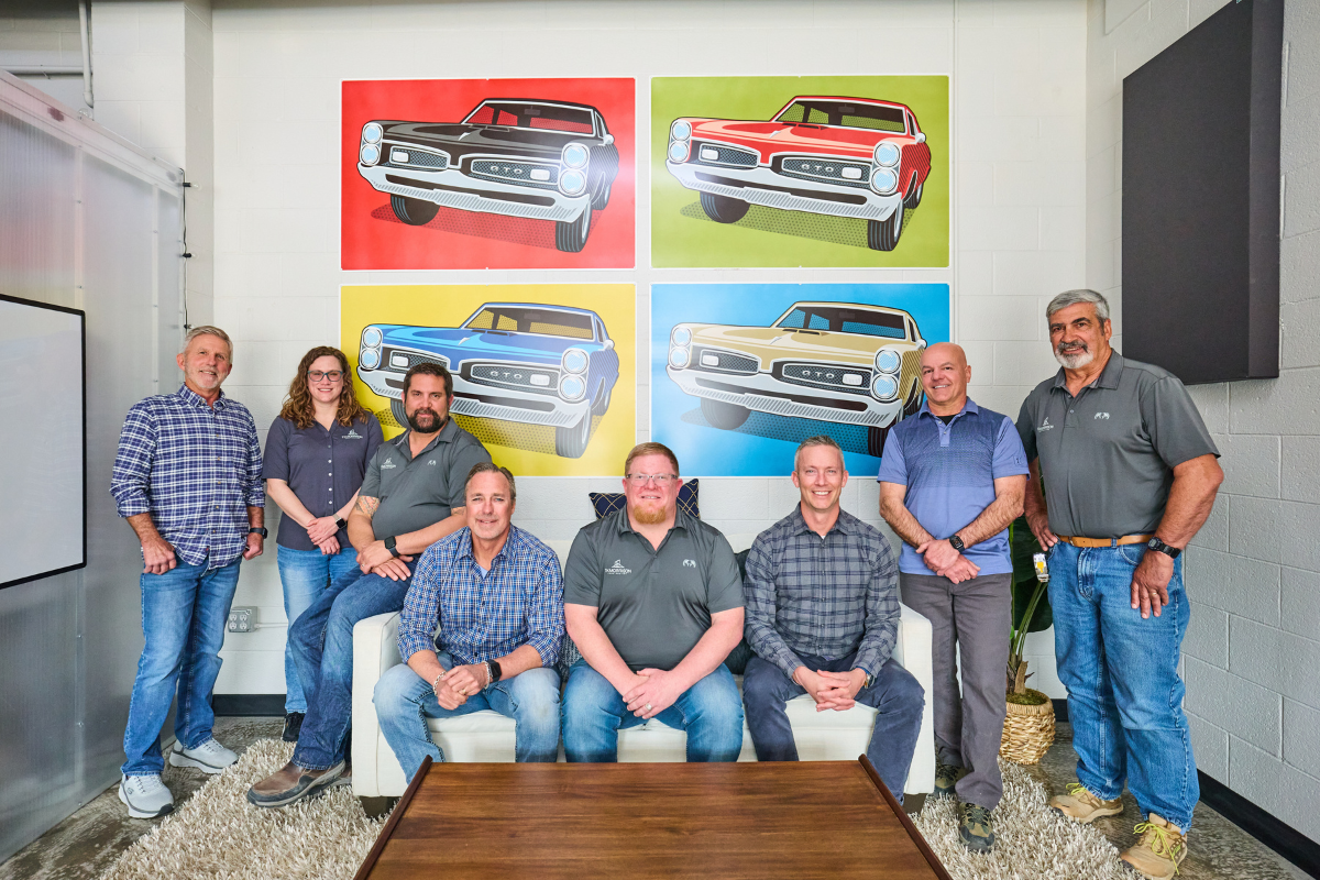 A photo of the TK Morrison team posing in front of a collage of classic cars in the background.