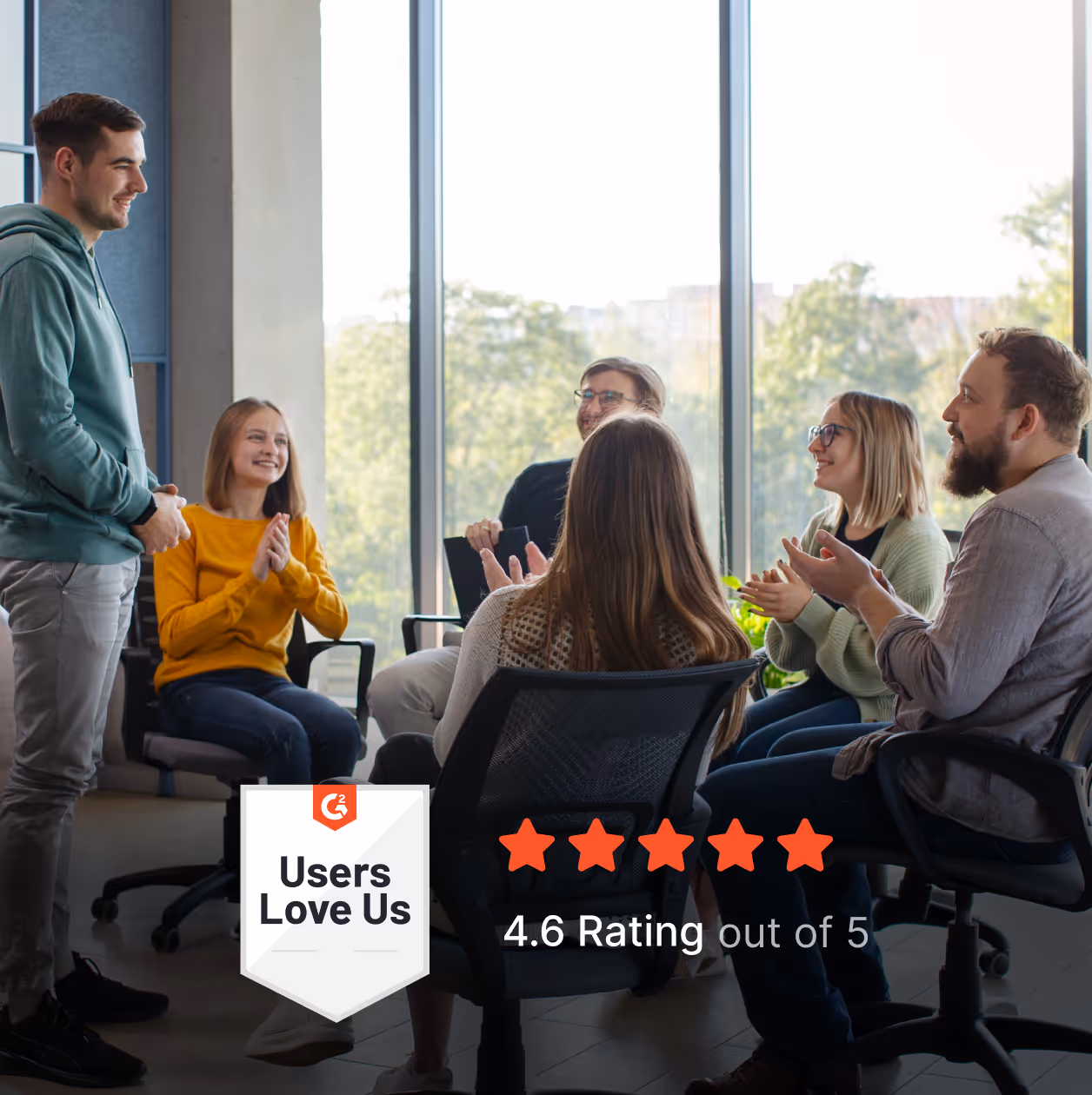 A small team having a collaborative discussion in a modern office, with people seated in a circle and applauding during a meeting.