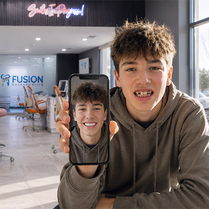 Teen boy in a cafe holding a phone displaying a smiling selfie of himself with braces.