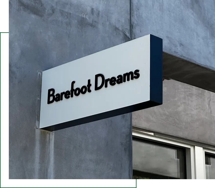 Exterior wall-mounted sign for Barefoot Dreams store on a gray concrete building