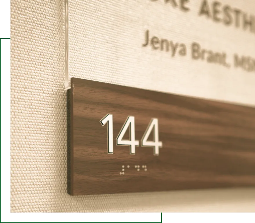 ADA-compliant room signage with number 144 and braille on wooden panel inside healthcare facility