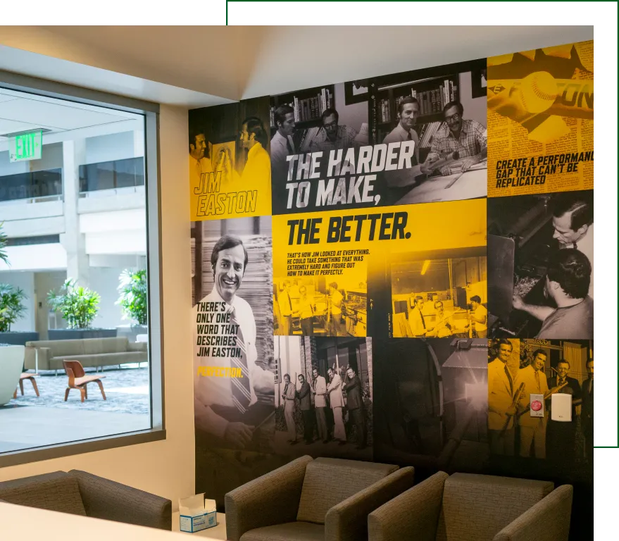 Corporate lobby wall mural featuring historical photos, bold typography, and branding message about innovation and excellence