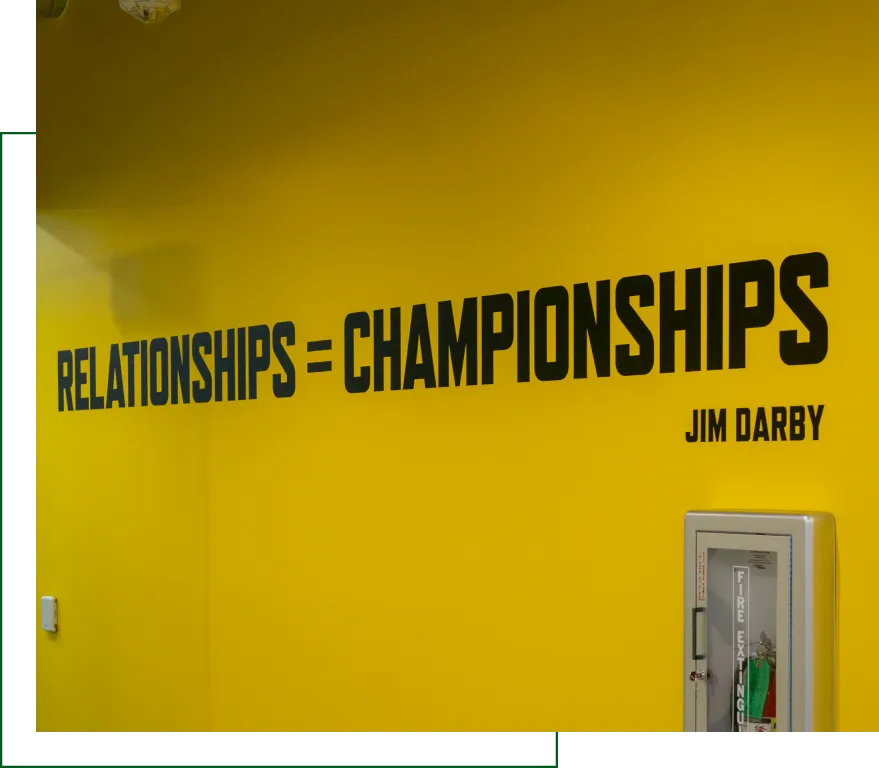Yellow office wall with bold black quote 'RELATIONSHIPS = CHAMPIONSHIPS' by Jim Darby above a fire extinguisher