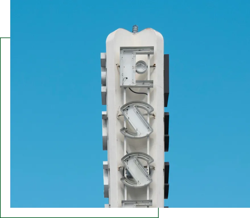Vertical exterior sign with large stylized letters against clear blue sky, representing institutional branding