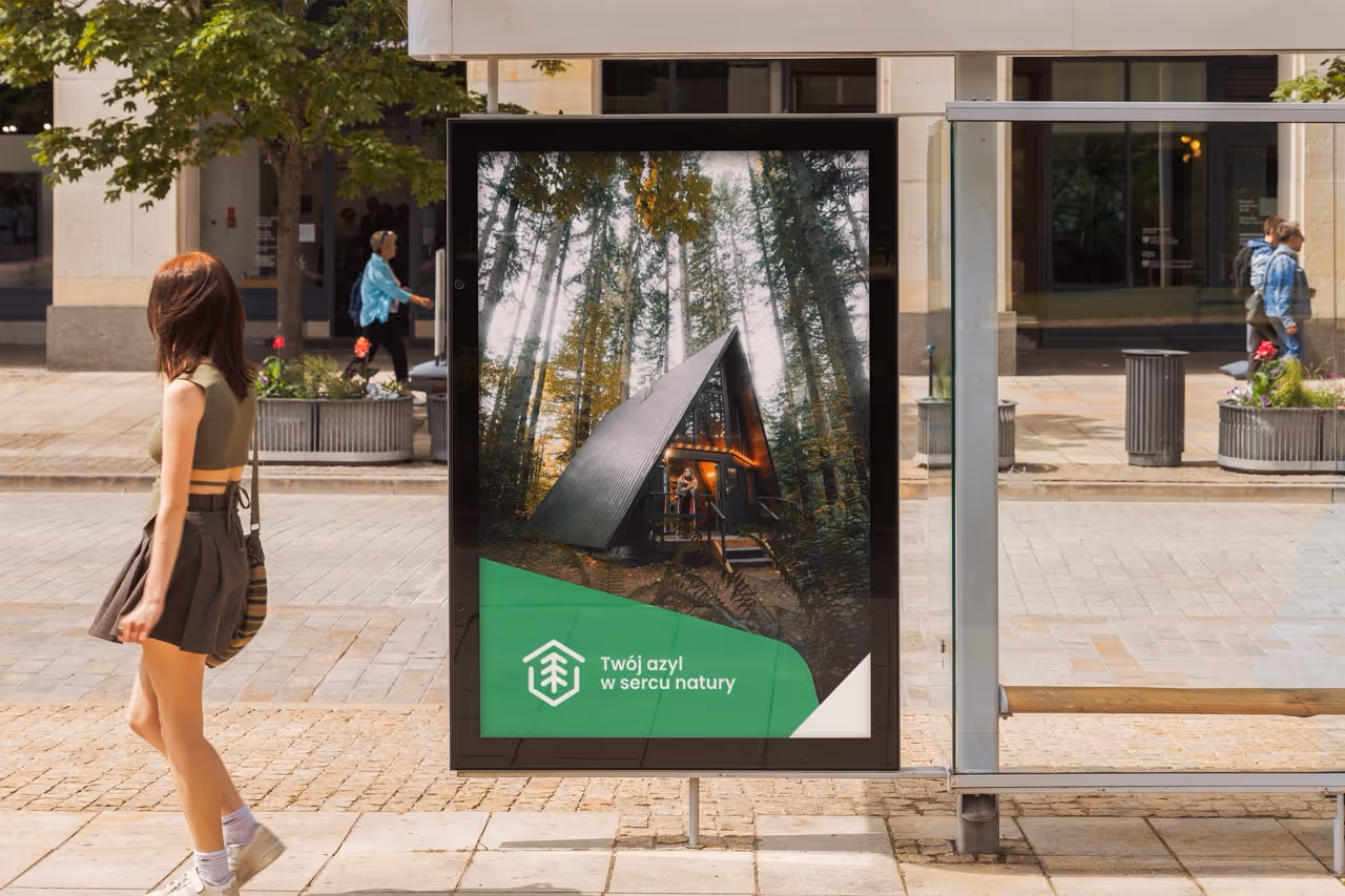 Przystanek autobusowy z reklamą drewnianego domku w lesie i napisem „Twój azyl w sercu natury”, z logo Cabinest