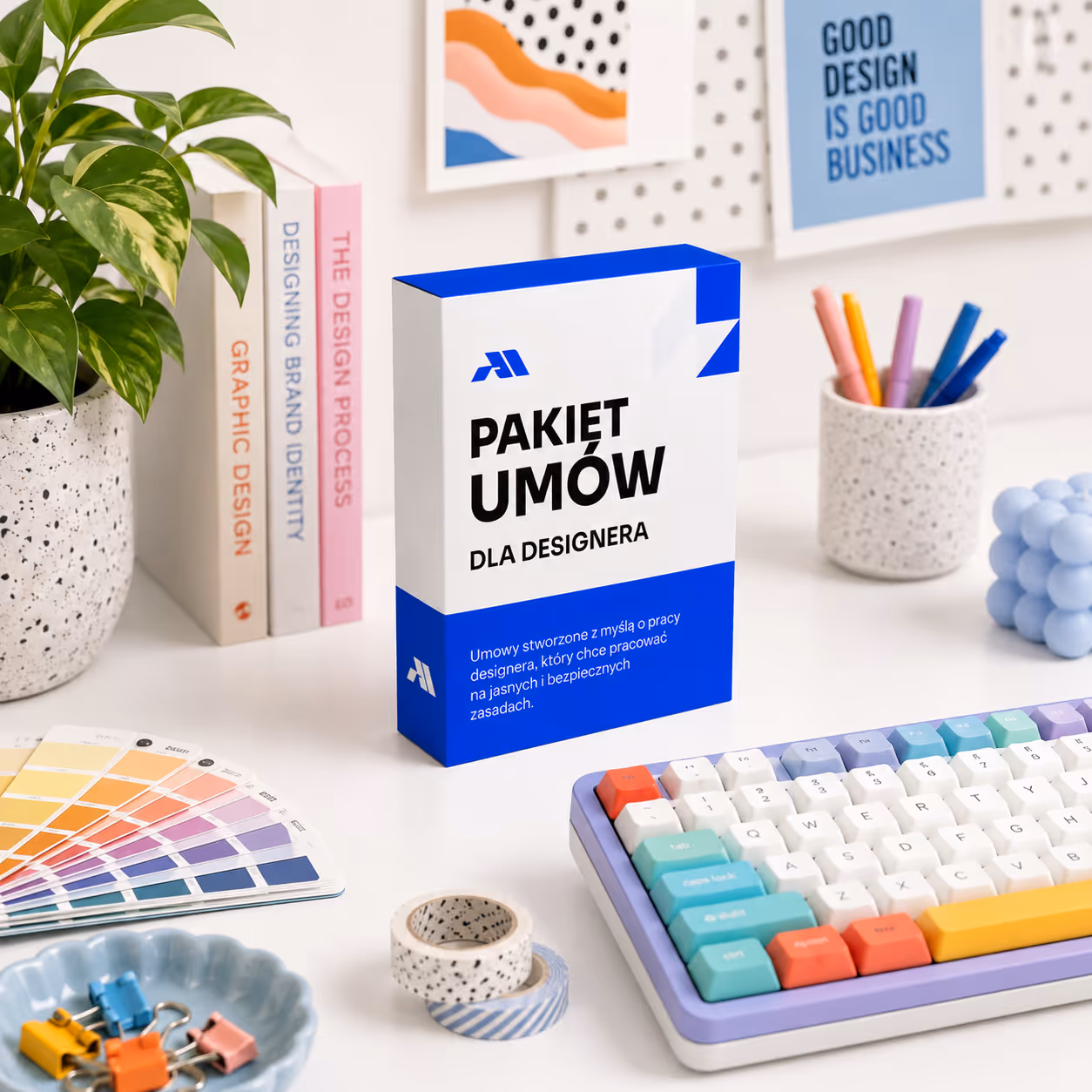 Pakiet umów dla designera stoi na biurku obok klawiatury, książek, próbek kolorów i rośliny.