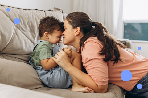 Mother and toddler touching foreheads on a sofa, connecting at eye level
