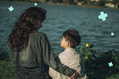 Mother and young son sitting together by a lake, boy looking up at her