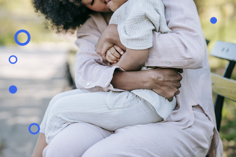 Mother holding her toddler close on a park bench, child nestled into her