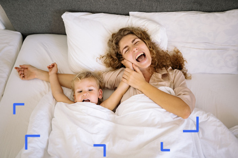 A tired mother lying in bed mid-yawn in the morning, her toddler stretching beside her
