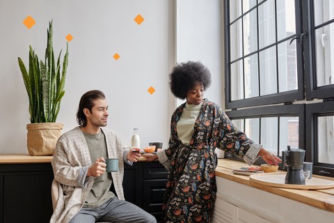 Couple in bathrobes having breakfast in a kitchen, standing apart and not touching