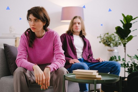 Woman sitting forward and looking away while her partner sits behind her on a sofa