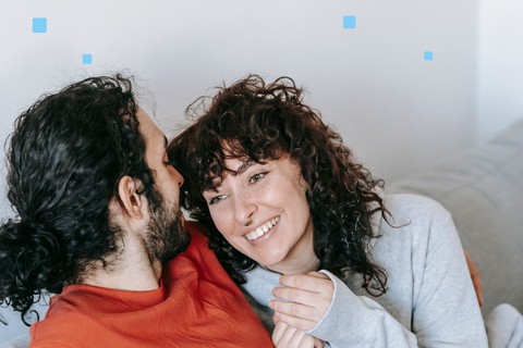 Couple sitting close on a sofa at home, woman smiling at her partner