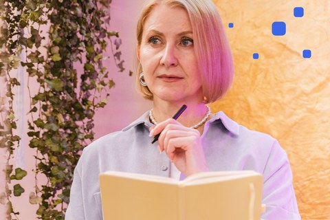 Woman in her forties holding an open notebook and a pen, thinking about what to write down