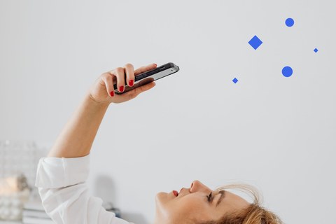 Woman leaning back holding her phone above her, against a plain light wall