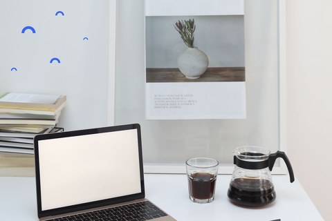 Laptop, coffee and a small notebook on a white desk in daylight