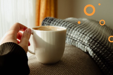 Hand holding a white mug of coffee by a sunlit window