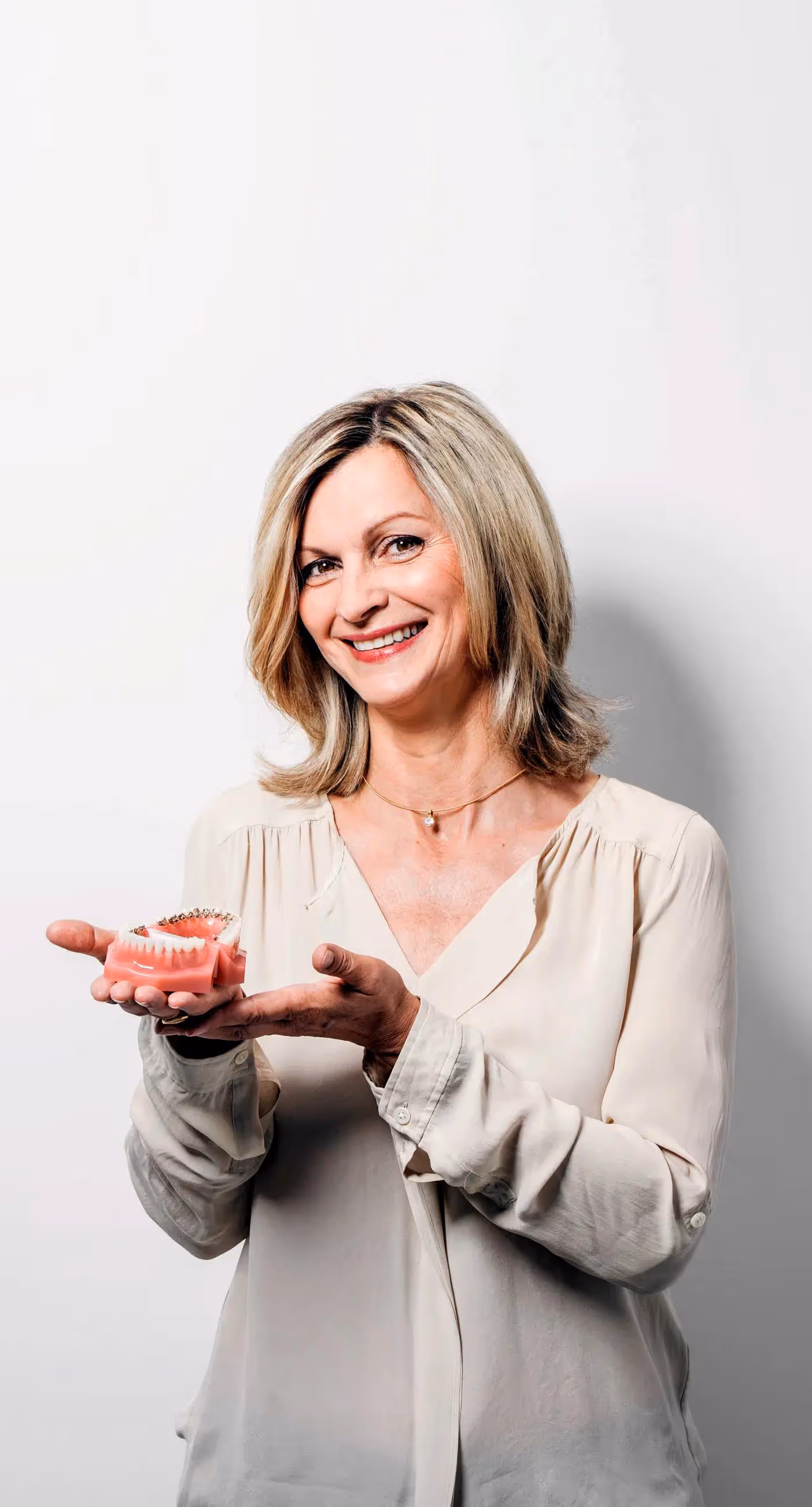 Lächelnde Frau hält ein zahnärztliches Modell mit Spangen in den Händen.