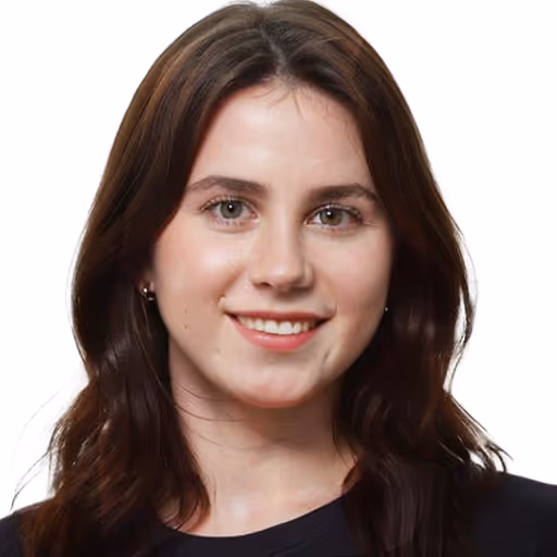 Junge Frau mit langen braunen Haaren, die lächelt und vor weißem Hintergrund steht.