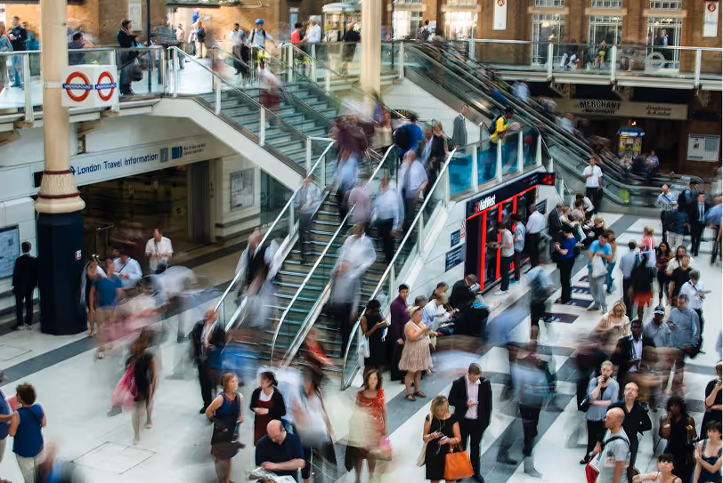 Busy London underground station with blurred people moving on stairs, escalators, and platform area.