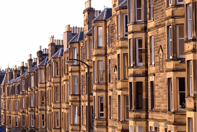 Row of old stone apartment buildings with bay windows and chimneys in warm light.