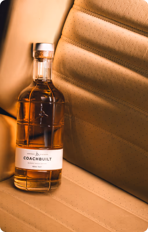 Bottle of Coachbuilt blended Scotch whisky placed on tan perforated leather car seat.