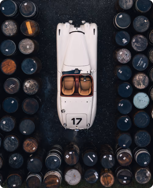 A white vintage racing car with the number 17 parked on a dark surface, surrounded symmetrically by old wooden barrels.