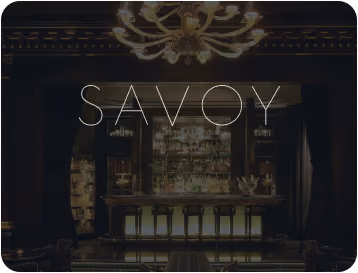 Elegant dimly lit bar area with a chandelier and stools, with the word 'SAVOY' overlayed in large letters.