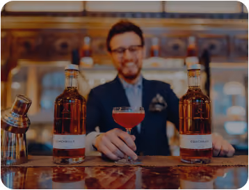 Bartender holding a cocktail glass with two bottles of Coachbuilt spirit on the counter.