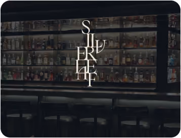 Bar interior with shelves fully stocked with various liquor bottles and stools lined up at the counter.