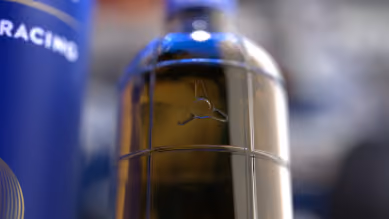 Close-up of a transparent bottle with a blue cap and logo featuring a three-pronged symbol.