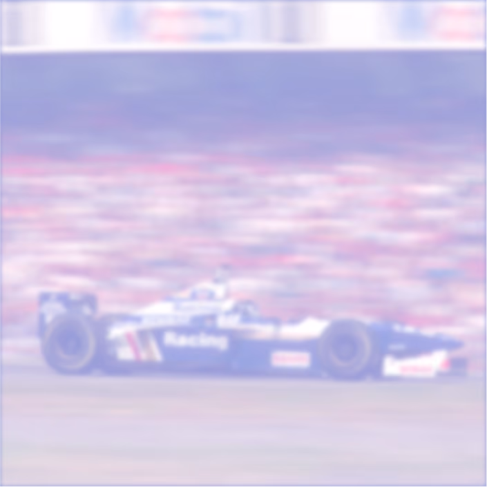 Vintage Formula 1 race car in blue and white with 'Racing' on the side, speeding on a racetrack with a blurred crowd in the background.
