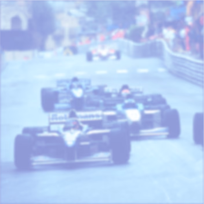 Blurred image of multiple Formula 1 race cars competing on a racetrack with spectators in the background.