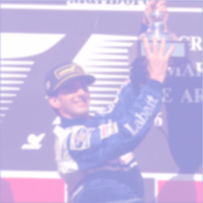 Race car driver in a blue suit and cap holding up a trophy on a podium.