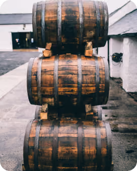 Stack of three wooden barrels outside a building with white walls.