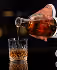 Hand pouring whiskey from a bottle into a glass with ice cubes on a black background.