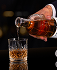 Hand pouring whiskey from a bottle into a glass with ice cubes on a black background.
