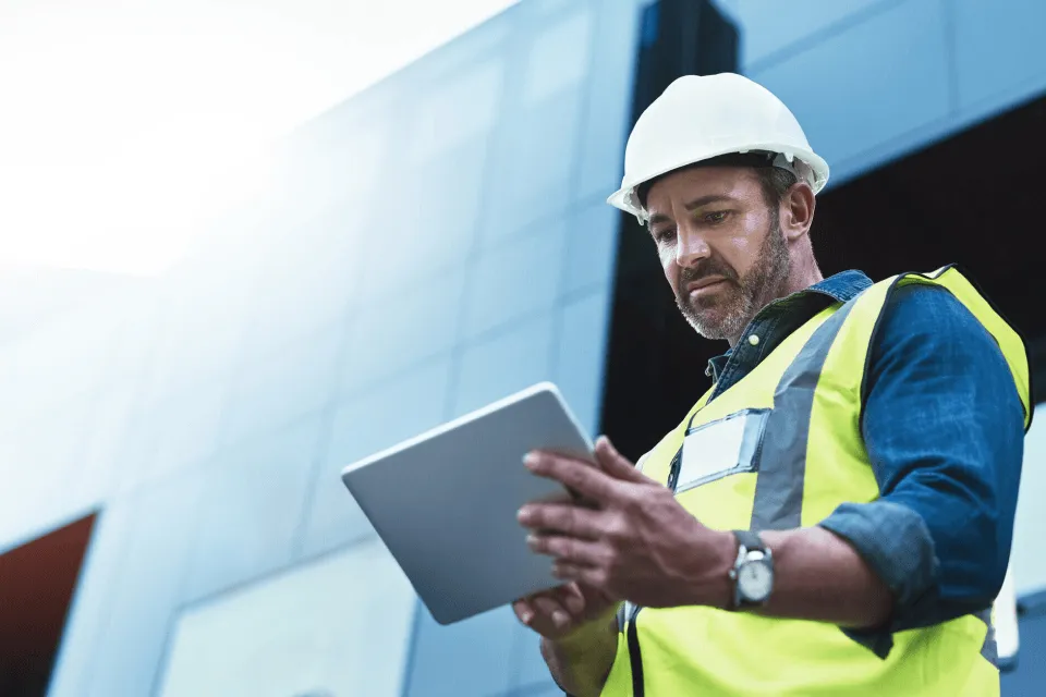 Building contractor wearing a hard had working on a tablet in front of new building