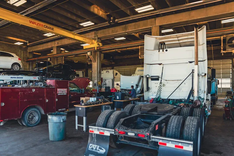 Fleet service showing heavy-duty trucks and service vehicles inside busy commercial repair shop with overhead crane.