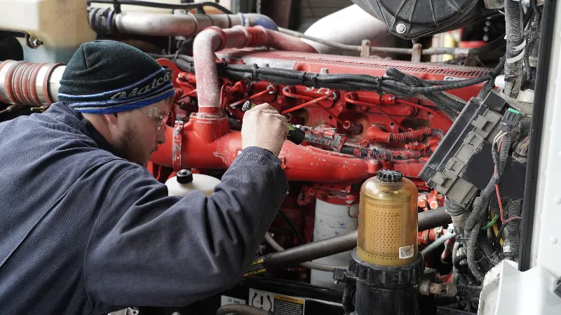Cummins engine service as a technician inspects wiring and components on a red diesel engine.