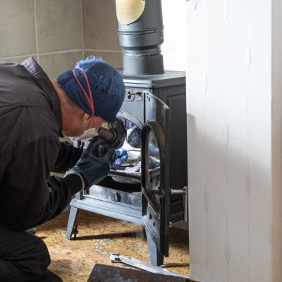 Technician inspecting a wood-burning fireplace stove to evaluate safety and performance.